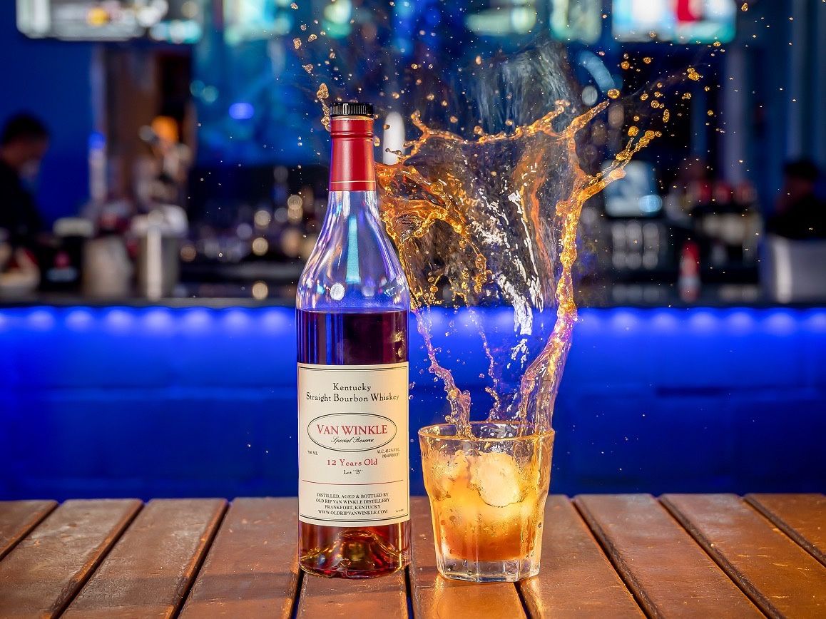 A bottle of Van Winkle 12 Year bourbon beside a splashing glass on the bar at Dive Bar Restaurant
