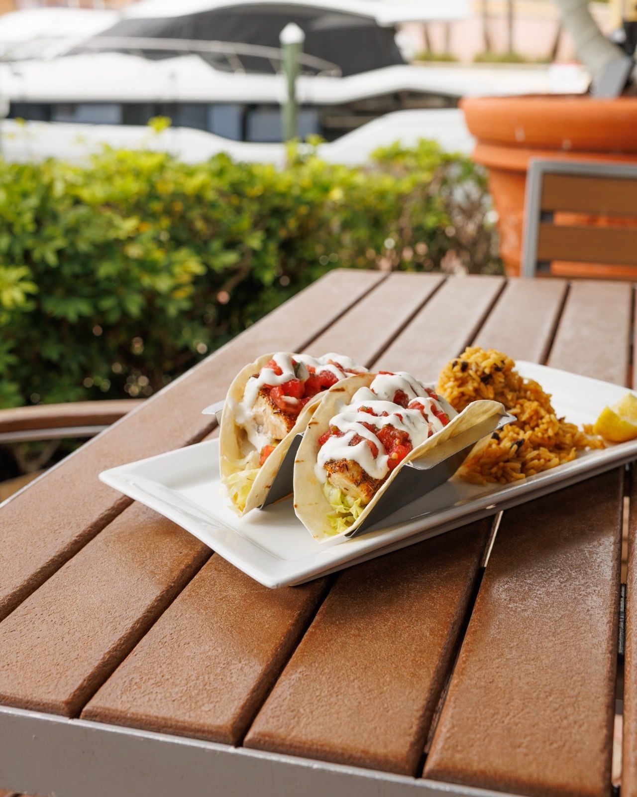 Blackened mahi tacos and rice on a patio table, with boats docked behind