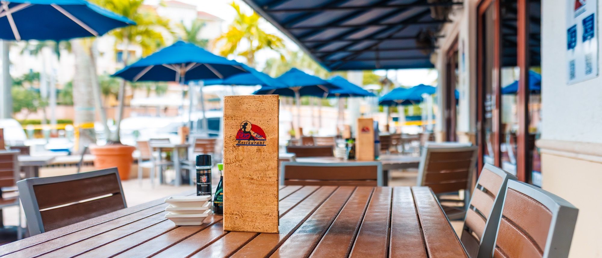 Patio tables under blue umbrellas, with a Dive Bar menu stand on the table